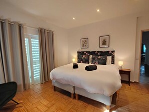 A hotel room with a large bed, two bedside lamps, a wooden floor, and a view of the hallway. - Casa Casuarina - Central private 3 bedroom villa  (Praia da Luz)