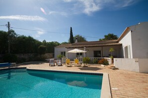 A swimming pool with lounge chairs and a patio area in front of a house with a tiled roof. - Casa Casuarina - Central private 3 bedroom villa  (Praia da Luz)