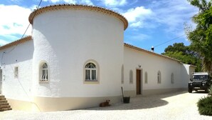 A white building with a curved facade, a door, and a small dog on the ground.