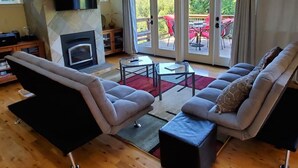 Una sala de estar con chimenea, un juego de sofá, una mesa de centro y vistas a un patio exterior con mobiliario rojo.