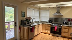 Una cocina con armarios de madera, una estufa y un lavabo. Hay una ventana con persianas, una puerta que da a un balcón y una pequeña mesa con sillas afuera.