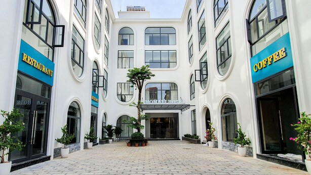A hotel with a central entrance, potted plants, and signs for a restaurant and coffee shop. - Momali Hotel Ninh Binh (Hoa Lu)