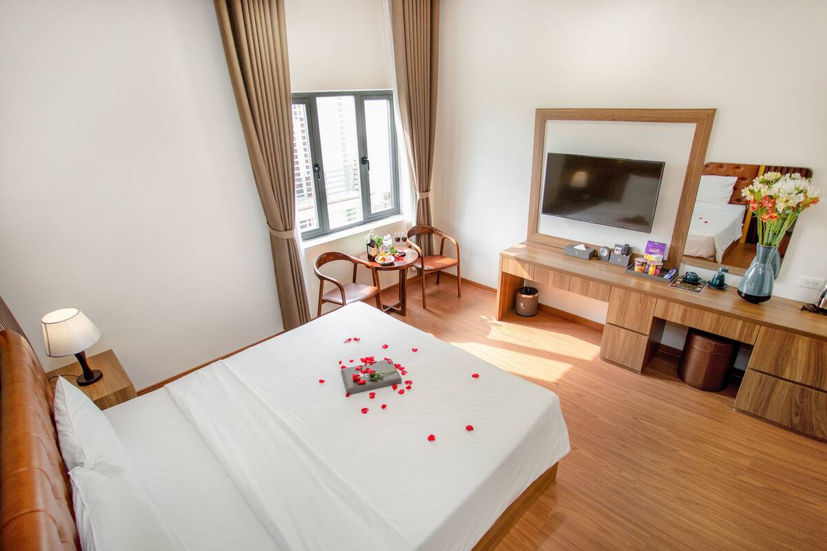 Habitación de hotel con cama, escritorio, silla, televisión y ventana con cortinas.