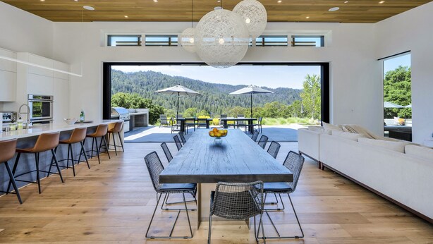 Una cocina moderna con una larga mesa de comedor, suelo de madera y vistas a las montañas.