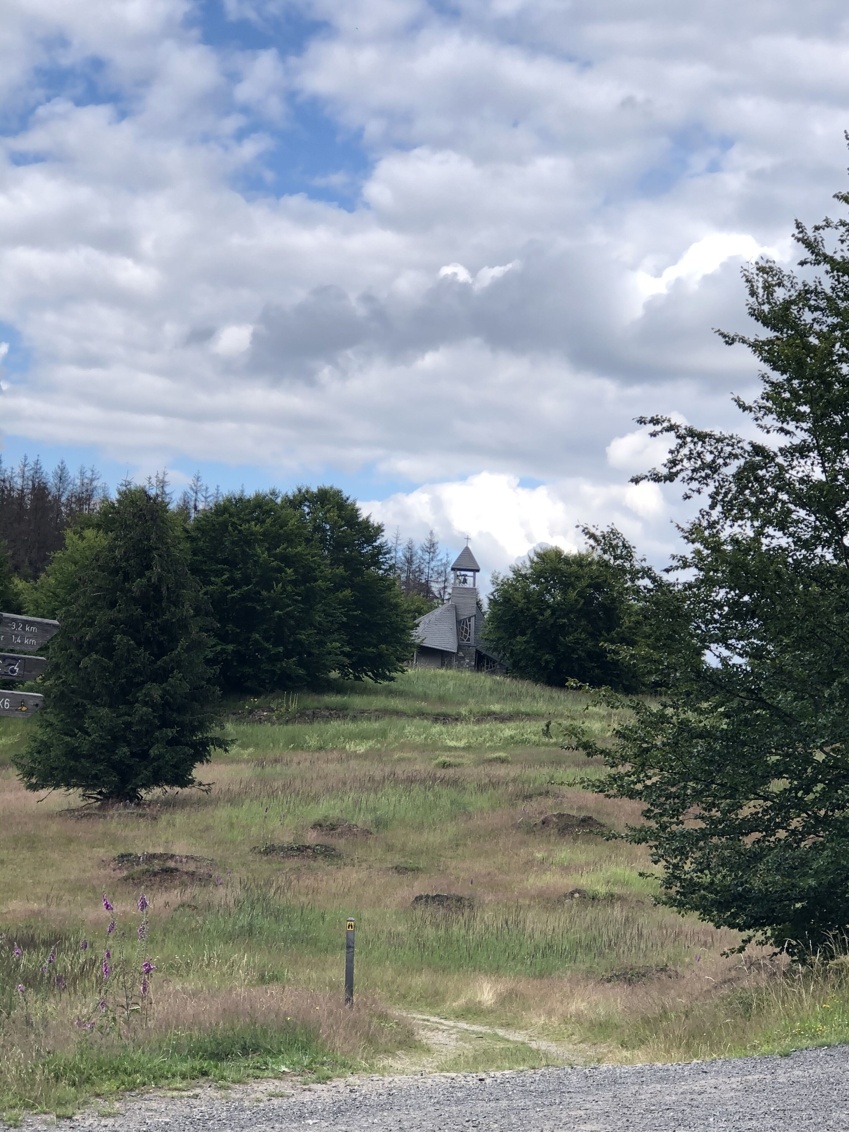 A rural landscape with a small church on a hill, surrounded by trees and grass.