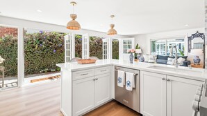 A modern kitchen with white cabinetry, a built-in dishwasher, and a large window overlooking a garden. - Balboa Island - Ruby Beach House
Steps from the beach. Sand in your toes. (Newport Beach)