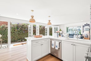 A modern kitchen with white cabinetry, a built-in dishwasher, and a large window overlooking a garden.