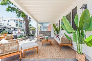 A covered outdoor seating area with wicker furniture, a coffee table, and large potted plants.