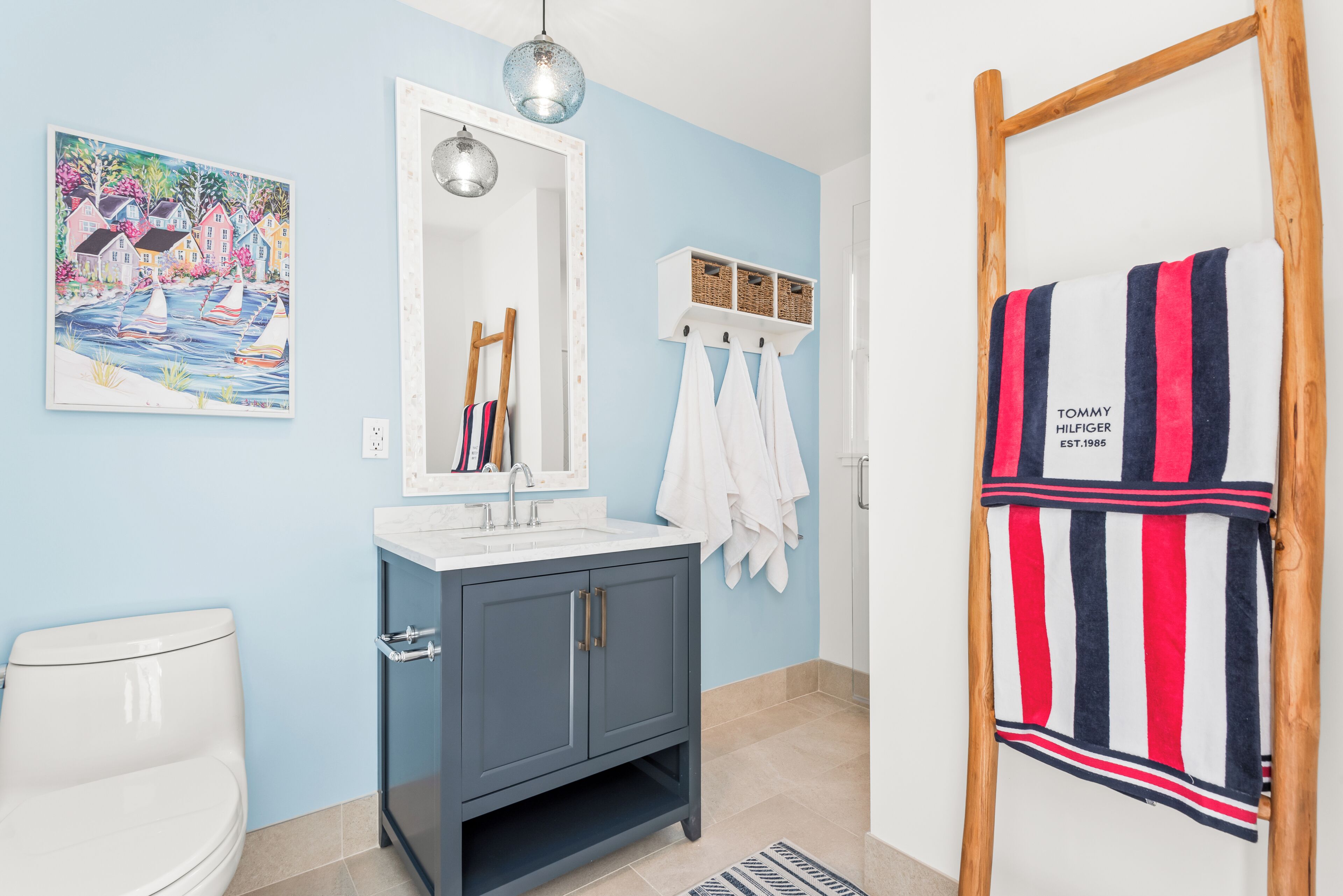 A bathroom with a white toilet, a blue cabinet, a mirror, a hanging towel rack, and a towel rack with a striped towel.