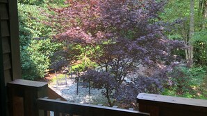 Terraza de madera con vista a un jardín que incluye un árbol de hojas moradas.