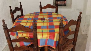A round wooden table with a colorful checkered tablecloth, surrounded by four wooden chairs with woven seats.