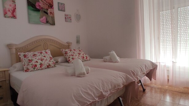 A bedroom with two beds, each with floral pillows and white linens. There are wall decorations including a heart and a 'LOVE' sign.