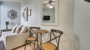 Ein Wohnzimmer mit einer Couch, zwei Holzstühlen, einem kleinen runden Tisch, einem Deckenventilator und einem an der Wand befestigten Fernseher.