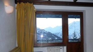 A cozy room with a plaid sofa, a wooden door with a view of snow-covered mountains, and a radiator. - Winter Holiday in Sestriere (Sestriere)
