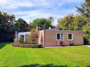 Una piccola casa in mattoni con un prato curato e un'area giardino con piante in vaso.