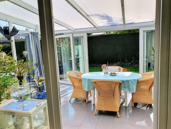 Una veranda con porta in vetro, mobili in vimini e un tavolo apparecchiato per la cena.