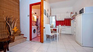 A compact kitchen with white cabinets, a dining area with a table and chairs, and a washing machine in the corner. - STELA - One Bedroom Apartment (Rovinj)