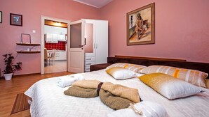 A bedroom with a bed, pillows, a painting, a potted plant, and a view of a kitchen and bathroom through an open door. - STELA - One Bedroom Apartment (Rovinj)