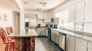 Een keuken met een centraal eiland, houten stoelen, witte kastjes, een magnetron en een vaatwasser.