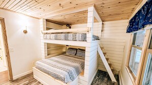 Een stapelbed met beddengoed met een patroon, houten wanden en een raam met gordijnen.