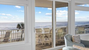 Een kamer met uitzicht op zee, een balkon met rieten stoelen en een blauw gestreept tapijt.