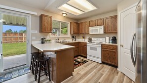 Una cocina con armarios de madera, un refrigerador blanco, un microondas y una estufa. Hay una zona con taburetes de bar y un felpudo.