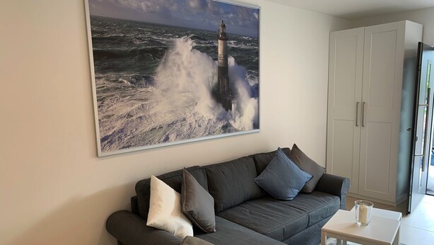 Een woonkamer met een grijze bank, een klein wit tafeltje en een groot schilderij van uitzicht op zee.