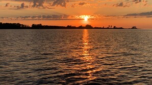 Een zonsondergang boven een wateroppervlak, met een silhouet van bomen en een landmassa in de verte.
