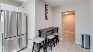 A modern kitchen with a stainless steel refrigerator, a dark wooden table with two bar stools, and a trash can.