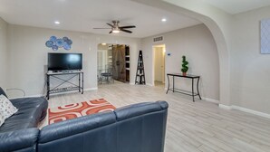 A living room with a sofa, a TV on a stand, a ceiling fan, and a staircase leading to another room.