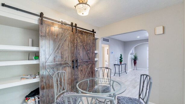 A dining area with a glass table and metal chairs, a wooden barn-style door, and a ceiling light fixture.