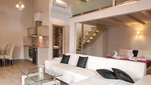 A modern living room with a white sofa, a glass coffee table, and a kitchen area with a built-in oven and sink. - Terezas Hotel (Corfu)