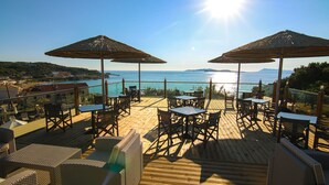 A wooden deck with outdoor seating and umbrellas overlooking a coastal view. - Terezas Hotel (Corfu)