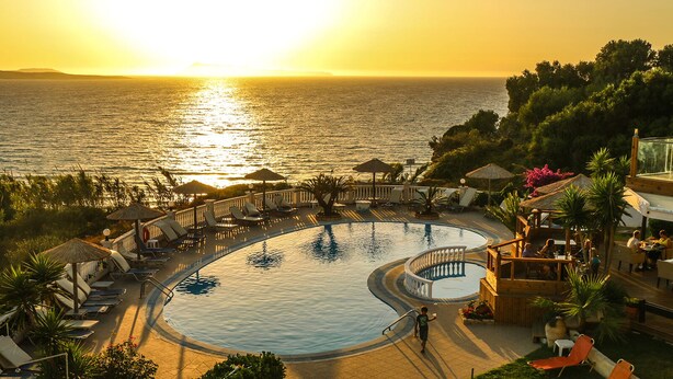 A resort pool with a view of the sunset over the sea, surrounded by lounge chairs and umbrellas. - Terezas Hotel (Corfu)