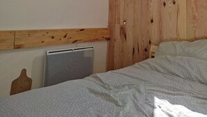 A bedroom with a wooden headboard, a large window, a radiator, and a bed with a patterned blanket. - Between Sainte Marie de Campan and La Mongie. (Campan)