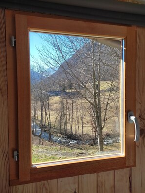 A wooden door with a window revealing a mountainous landscape, a door handle, and a metal latch.