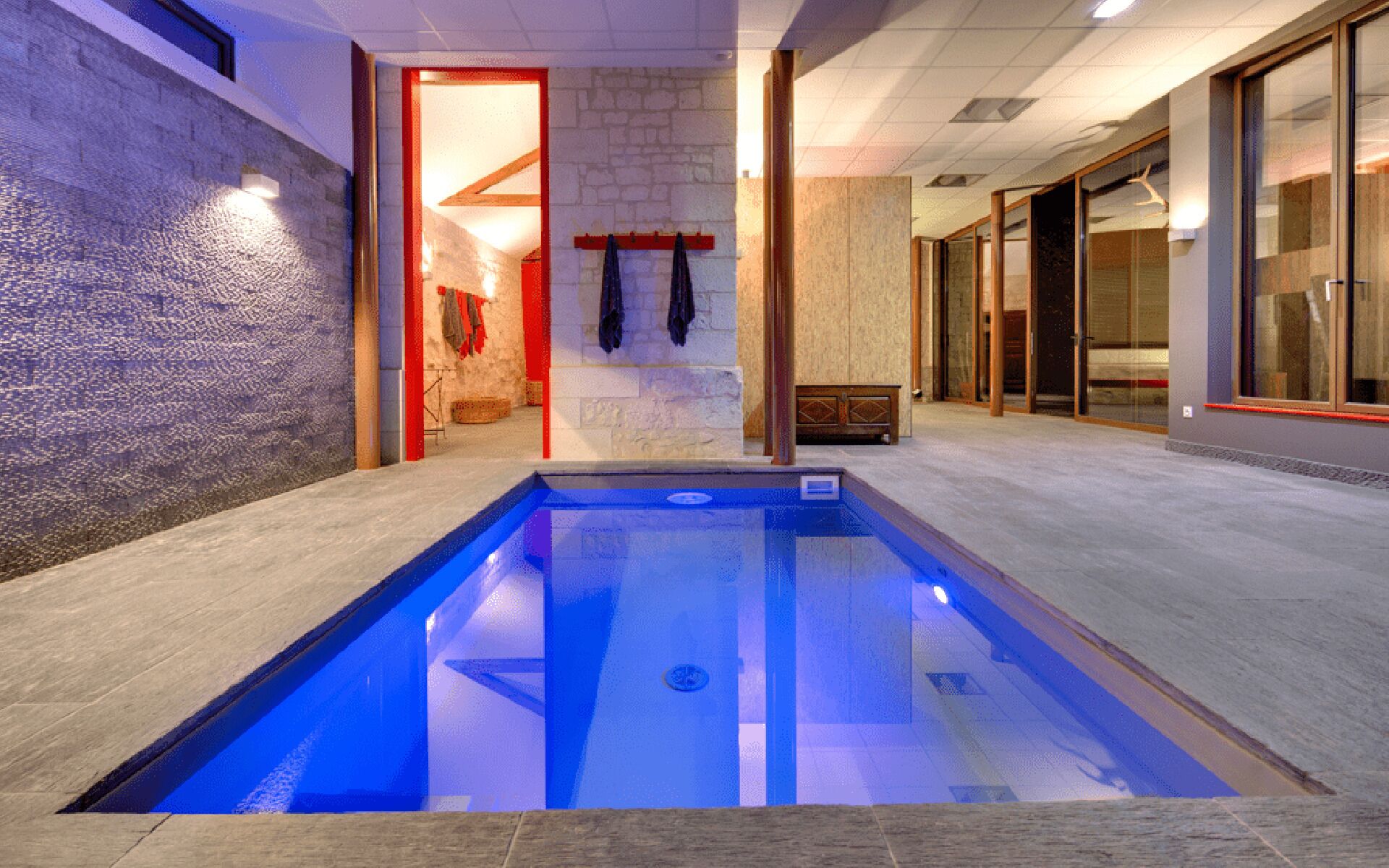 A swimming pool with a stone wall and a wooden bench.