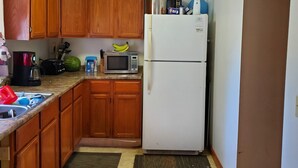 A compact kitchen with wooden cabinets, a microwave, a refrigerator, and a countertop with various appliances and items. - Sunset cottage complete w/large deck, fire pit and mins away from public beach (Lake Milton)