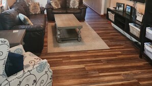 A living room with a sofa, a coffee table, a TV, and a ceiling fan. - Sunset cottage complete w/large deck, fire pit and mins away from public beach (Lake Milton)