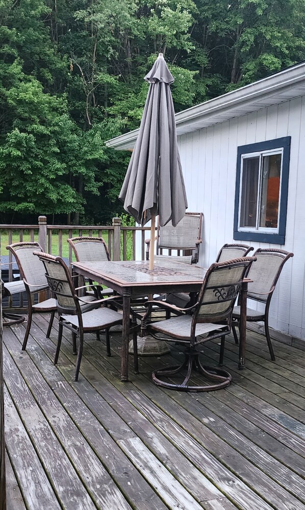 A wooden deck with a table and chairs, an umbrella, and a white building with a window in the background.