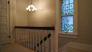 A staircase with white balusters and a black handrail, leading to a room with a window featuring stained glass with floral designs.