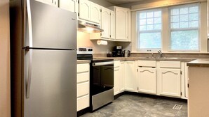 A kitchen with white cabinets, a stainless steel refrigerator, a stove, and a window with blinds. - Charming Colonial Home with Private Chipping Green (Hutchinson)