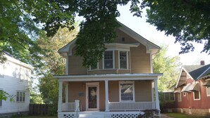 A two-story house with a front porch, a small front yard, and a wooden fence. - Charming Colonial Home with Private Chipping Green (Hutchinson)