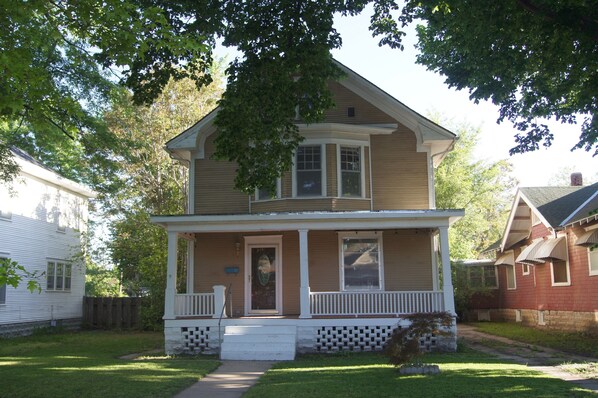 A two-story house with a front porch, a small front yard, and a wooden fence. - Charming Colonial Home with Private Chipping Green (Hutchinson)