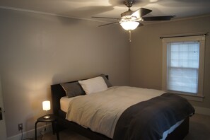 A bedroom with a bed, a ceiling fan, a bedside lamp, and a window with blinds. - Charming Colonial Home with Private Chipping Green (Hutchinson)