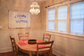 A dining room with a round wooden table, four wooden chairs, a chandelier, and a whiteboard with "WELCOME TO MUTH" written on it. - Charming Colonial Home with Private Chipping Green (Hutchinson)