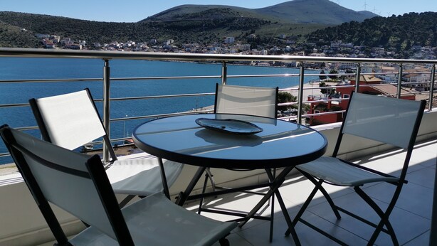 A balcony with a round table and chairs overlooking a body of water and a town.