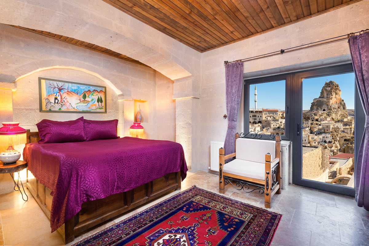 A bedroom with a large bed, a view of a cityscape, a painting on the wall, and a wooden ceiling.