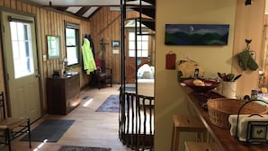 A cozy interior with wooden walls, a staircase, a dining area with a table and chairs, and a kitchen counter with various items.