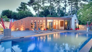 Un área de piscina moderna con estructura de madera, sillones de descanso y una piscina cristalina.